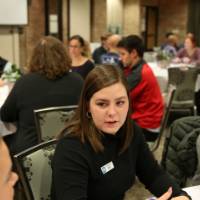 A student shares her thoughts at a table discussion while two students listen intently